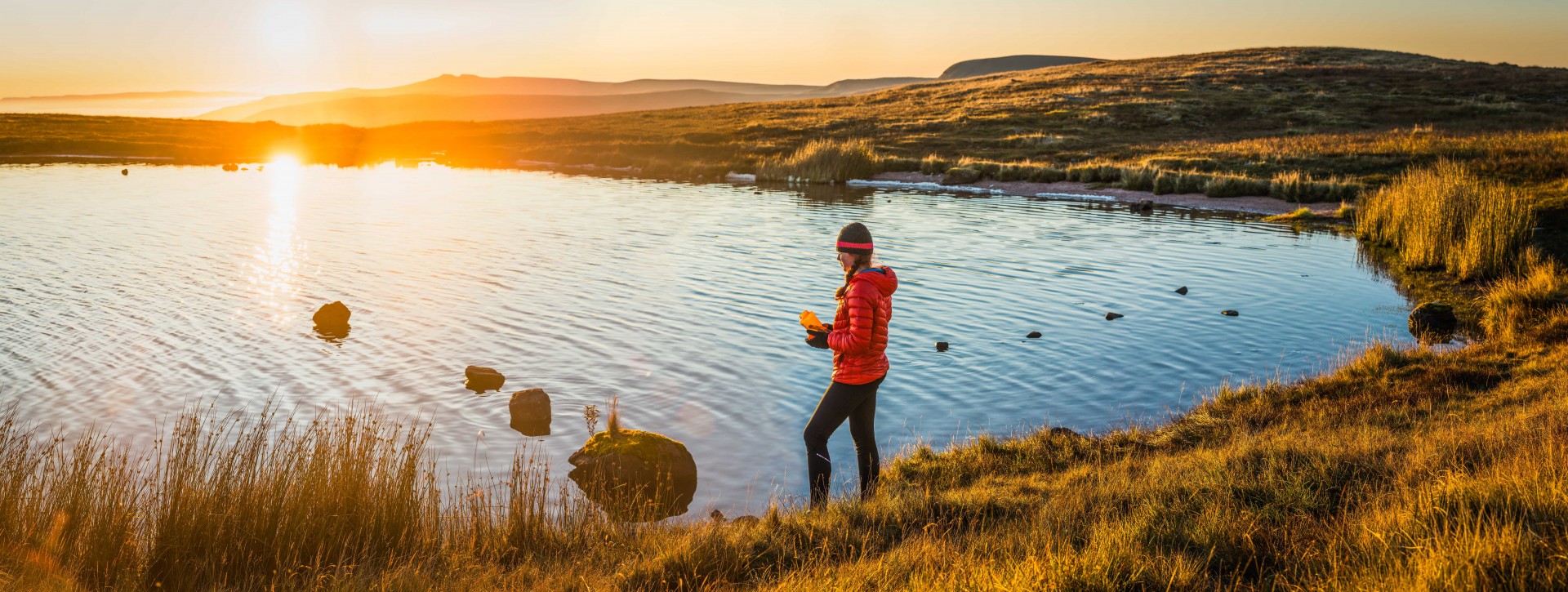 Female hiker filling water bottle from mountain lake sunrise